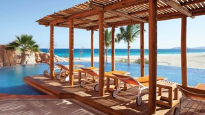 Une terrasse en bois avec des chaises longues et une piscine donnant sur une plage.