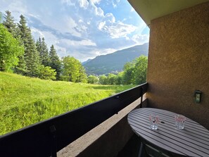 Un balcone con un tavolo e due bicchieri, vista su un prato e una montagna.
