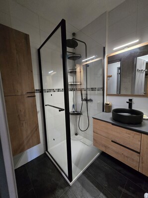 Un baño moderno con ducha de vidrio, tocador de madera y un espejo grande.