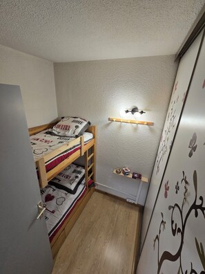A small, compact room with a bunk bed, a wall-mounted shelf with toys, and a door with a floral design. - South-facing mountain apartment: summer/winter ideal for biking, climbing, hiking and skiing (Briançon)