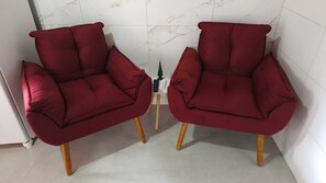 Deux fauteuils rouges aux pieds en bois, placés dans un coin d’une pièce aux murs de marbre blanc.