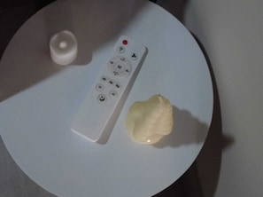 Eine weiße Fernbedienung auf einem weißen Tisch, neben ihr ein kleines, weißes Objekt.