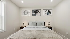 A bedroom with a bed, two nightstands, a wall-mounted light fixture, and three framed wall art pieces.