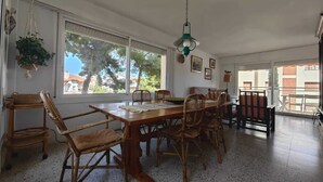 Ein Essbereich mit Holztisch und Korbstühlen, großen Fenstern mit Blick auf Bäume und einer hängenden Pflanze.