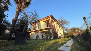 Una casa de dos pisos con un balcón, rodeada de árboles y una cerca de malla metálica.
