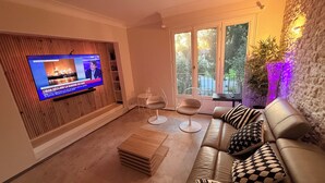 Una sala de estar moderna con televisor, un sofá, dos sillones y vistas al exterior a través de un ventanal grande.