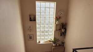 Un pasillo estrecho con una ventana, un reloj y una planta pequeña en un estante.