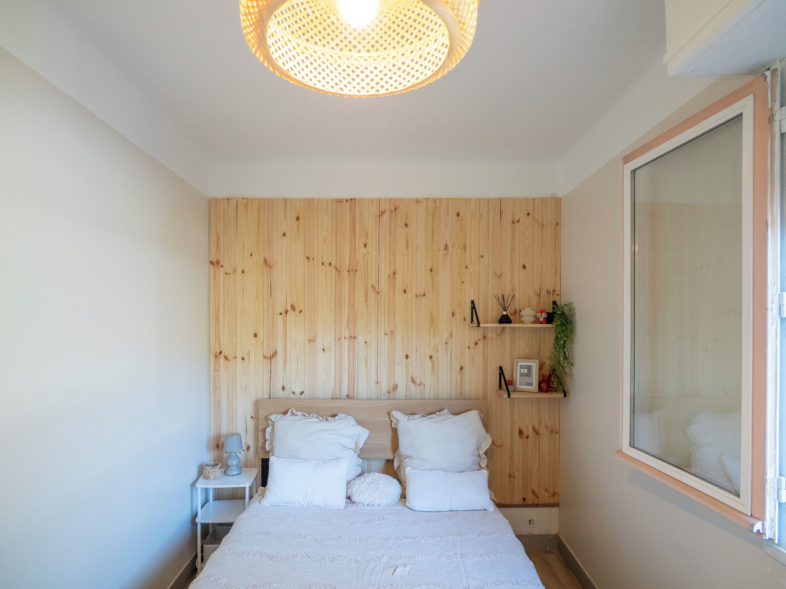 Une chambre avec un mur lambrissé en bois, un lit avec une literie blanche, une table de chevet avec une lampe et une fenêtre donnant sur un beau paysage.