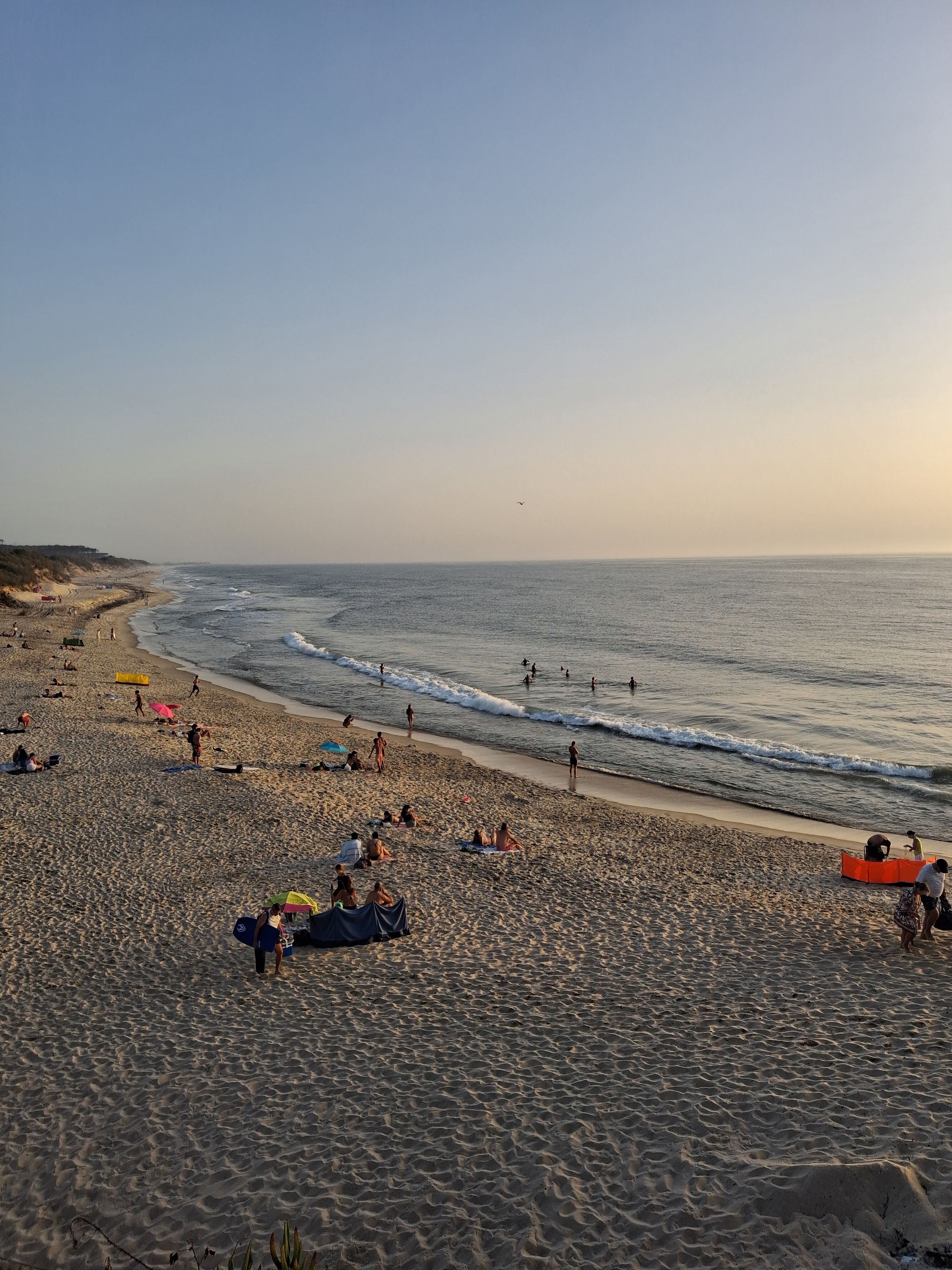 Uma praia com pessoas tomando sol e nadando, com céu claro.