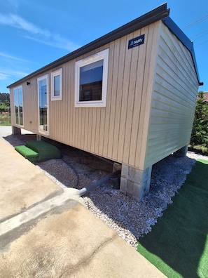 A mobile home with a nameplate, windows, and a gravel foundation.