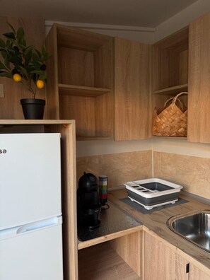 A compact kitchen with wooden cabinets, a white refrigerator, a coffee maker, a basket, and a sink. - Modular Refuge - between the pine forest and the sea (Maceda)