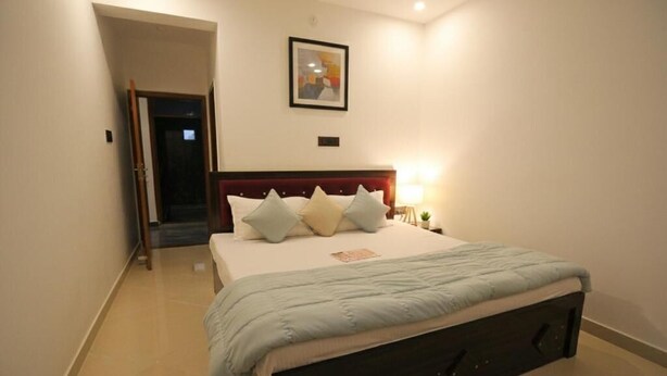 A bedroom with a bed, pillows, a nightstand, a lamp, and a framed picture on the wall. - Monishka Palace  (Faizabad)