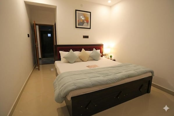 A bedroom with a bed, pillows, a nightstand, a lamp, and a framed picture on the wall. - Monishka Palace (Faizabad)