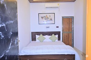 A room with a bed, a wooden door, a wall-mounted air conditioner, and a framed geometric artwork. - Monishka Palace  (Faizabad)