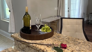 Uma bancada de cozinha com uma garrafa de vinho, copos de vinho e um prato de uvas.