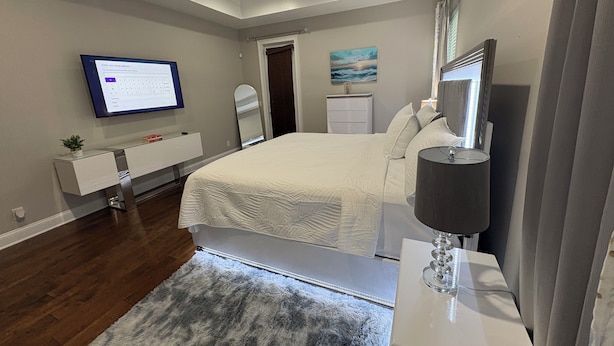 Quarto moderno com cama, mesa de cabeceira, televisão e ventoinha no teto.