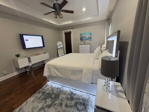 Un dormitorio moderno con cama, mesita de noche, televisor y ventilador de techo.