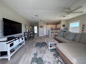 Ein Wohnzimmer mit Fernseher, Sofa, Couchtisch und einer Küche im Hintergrund.