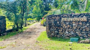 A stone wall with 'TE NUNOA' carved on it, a dirt path, and lush greenery. - Villa Te Nunoa - Polynesian Villa w/ Salt Water Pool (Haapiti)