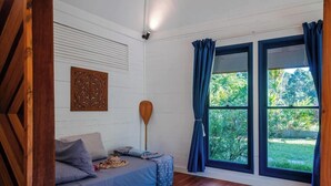 A room with a bed, a wooden paddle, a wall-mounted decorative panel, and large windows with curtains. - Villa Te Nunoa - Polynesian Villa w/ Salt Water Pool (Haapiti)