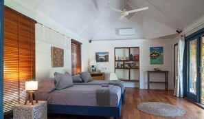 A bedroom with a bed, bedside tables, a nightstand, a bookshelf, and a window with blinds. - Villa Te Nunoa - Polynesian Villa w/ Salt Water Pool (Haapiti)