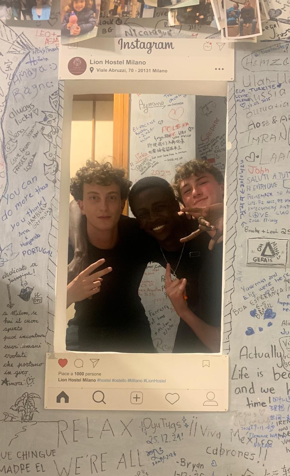 Een muur met verschillende teksten en tekeningen, waaronder namen en data, en een ingelijste foto van drie personen.