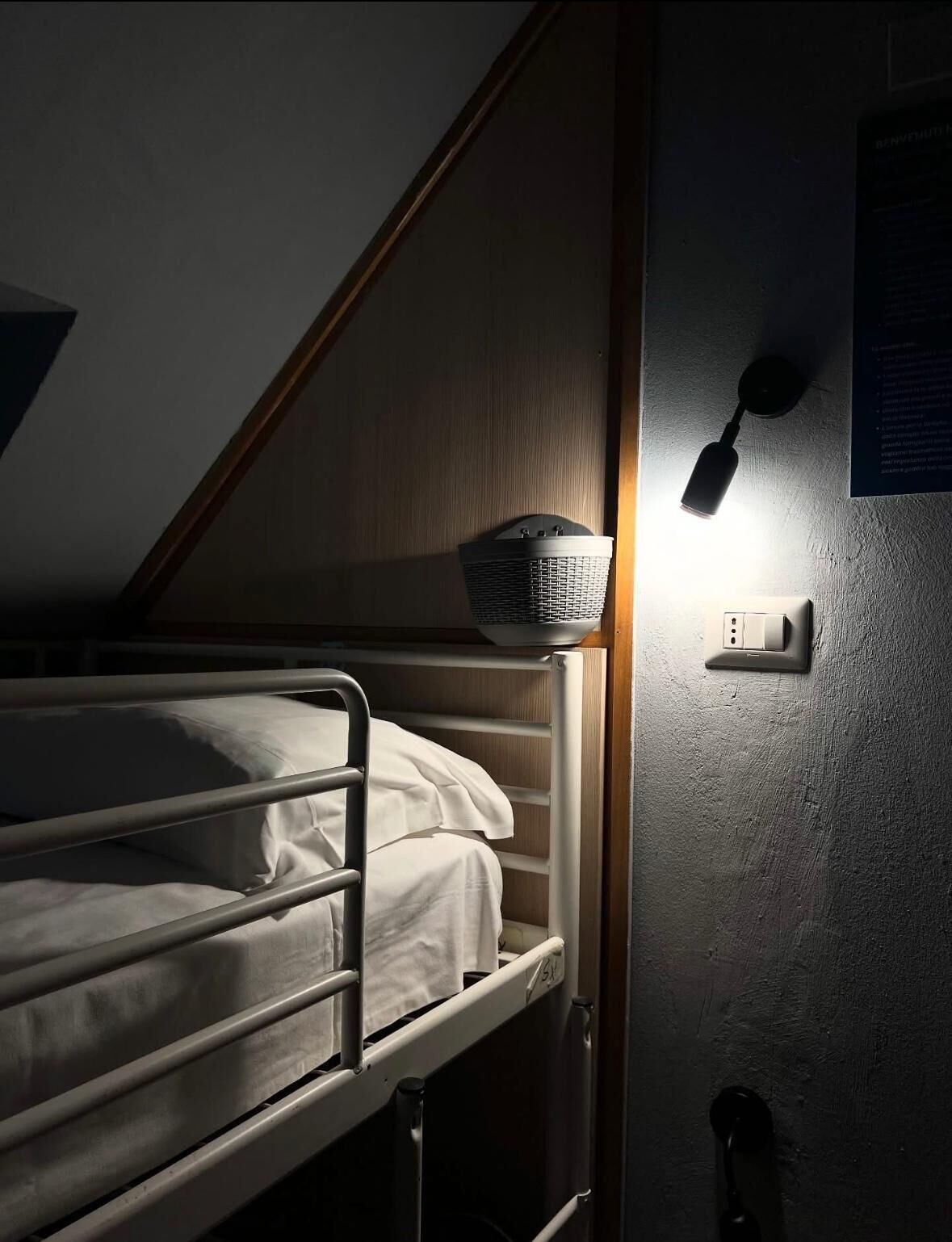 En våningssäng med en sänggavel, en väggmonterad lampa och ett eluttag.