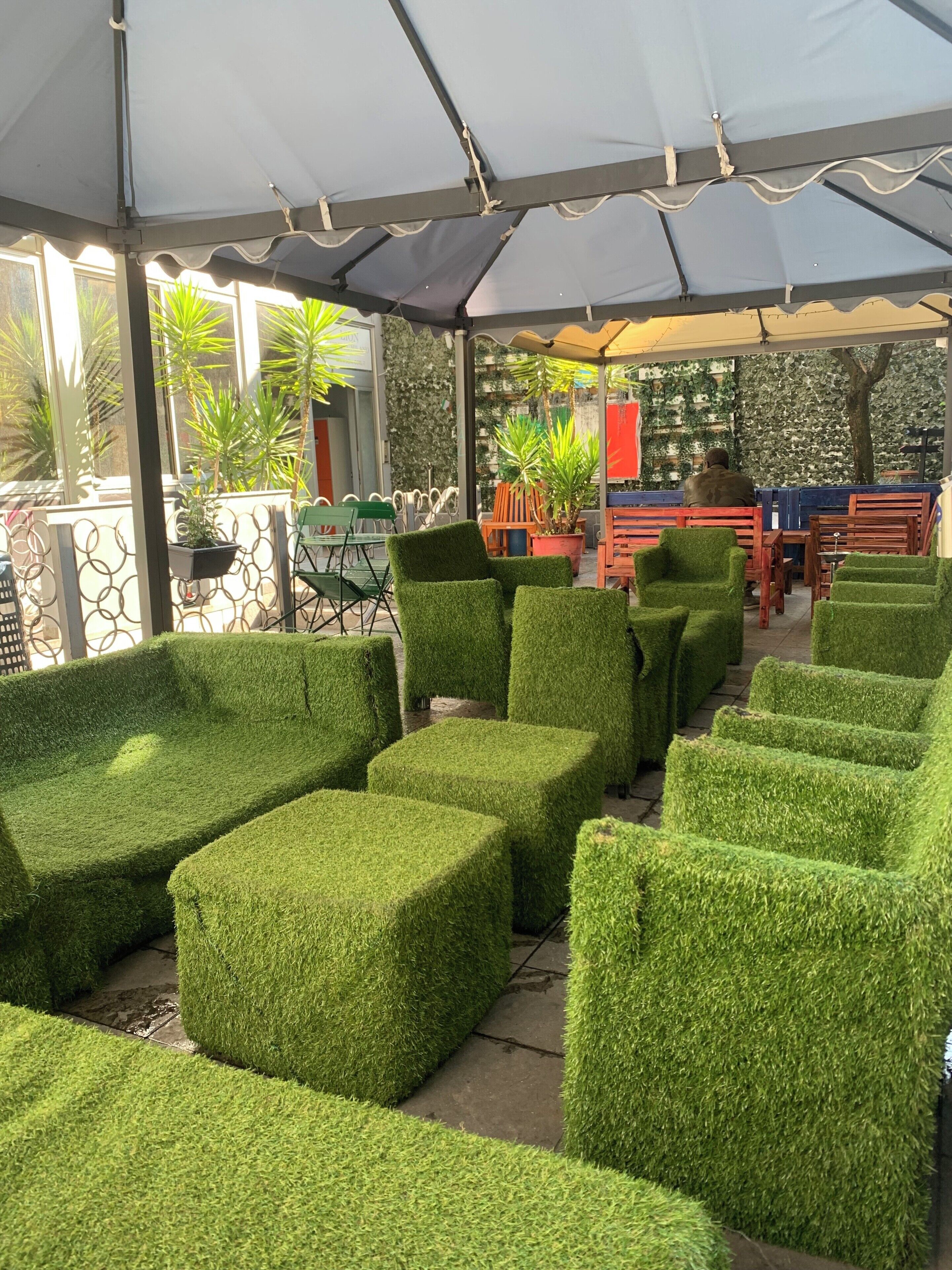 A covered outdoor seating area with artificial grass furniture and potted plants.
