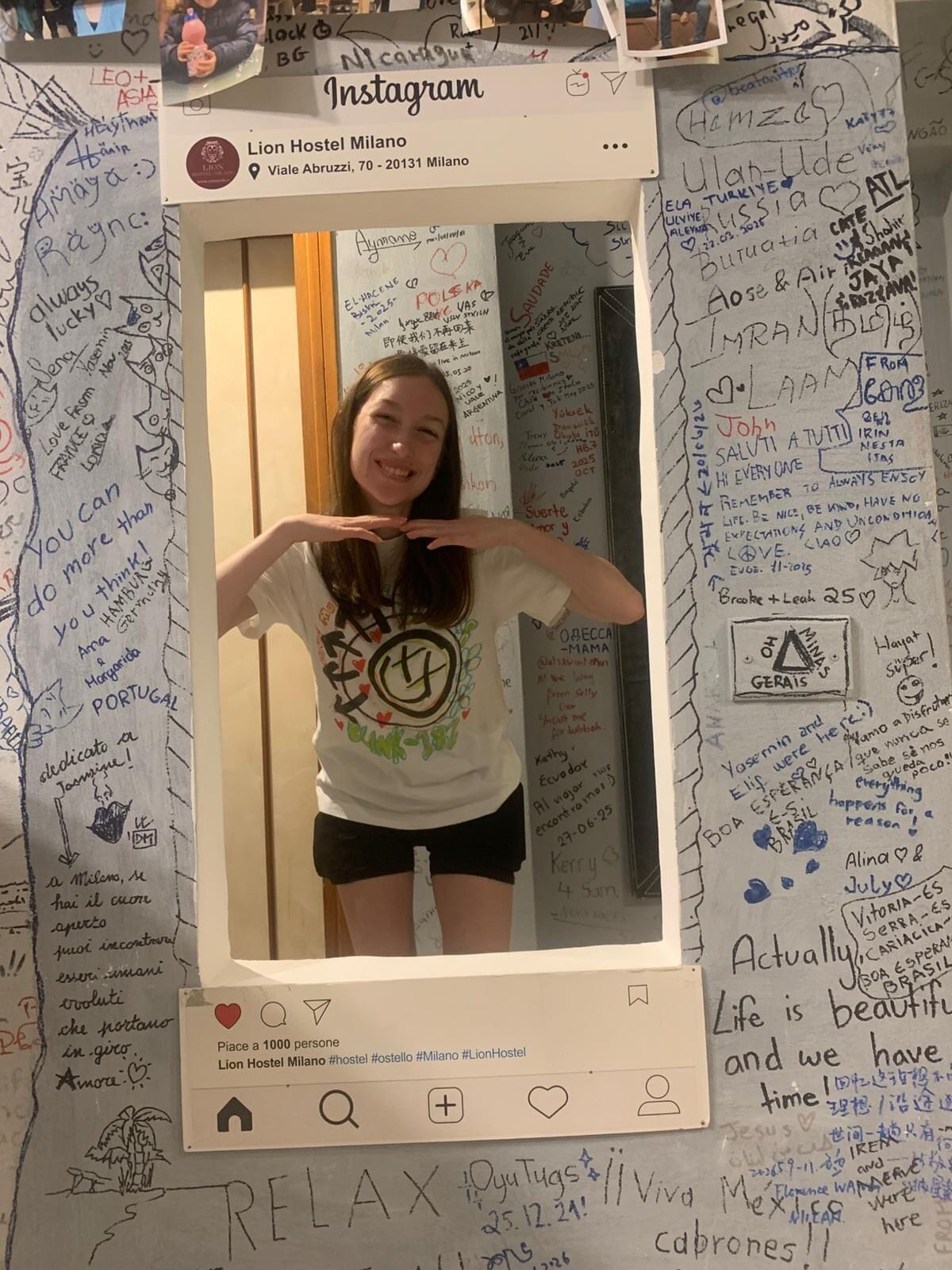 Um selfie com uma parede coberta de anotações e desenhos escritos à mão, moldura branca com legenda do Instagram e hashtag para o Lion Hostel Milano.