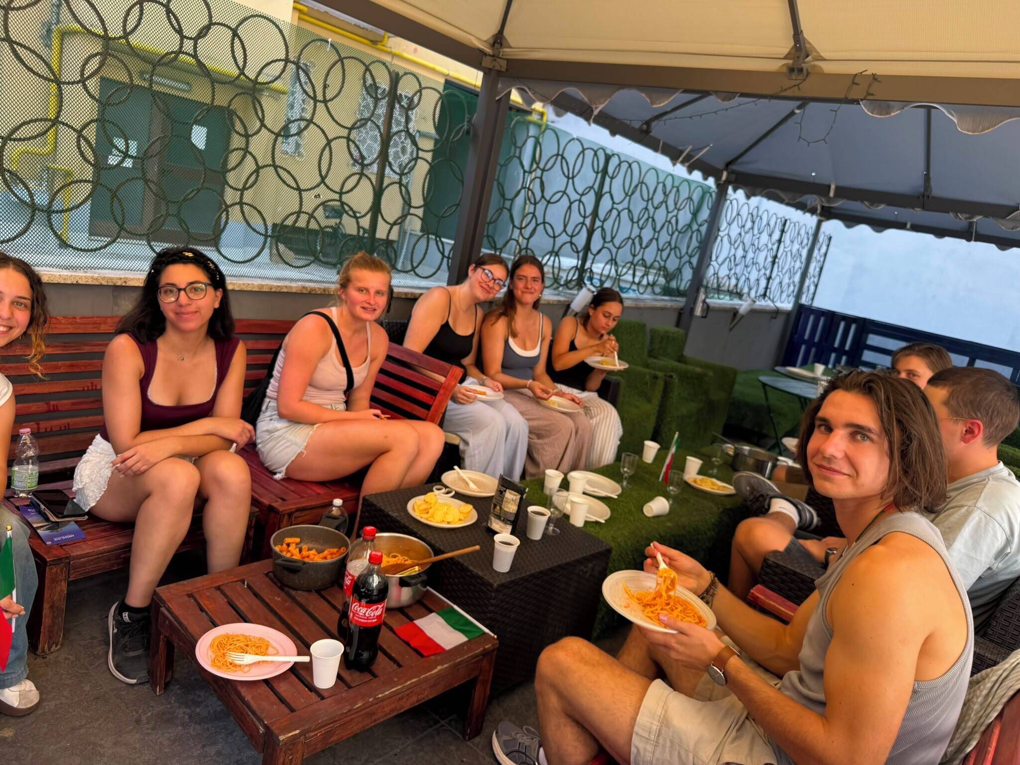 Un grupo de personas cenando al aire libre, con mesas y sillas, una botella de Coca-Cola y platos de comida.