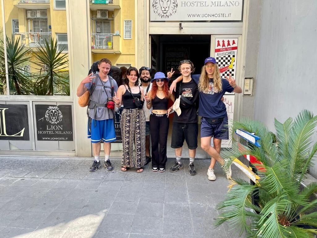 Een groep mensen poseert voor een gebouw met een logo van een leeuw en de tekst 'LION HOSTEL MILANO'.