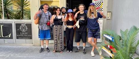 Een groep mensen poseert voor een gebouw met een logo van een leeuw en de tekst 'LION HOSTEL MILANO'.