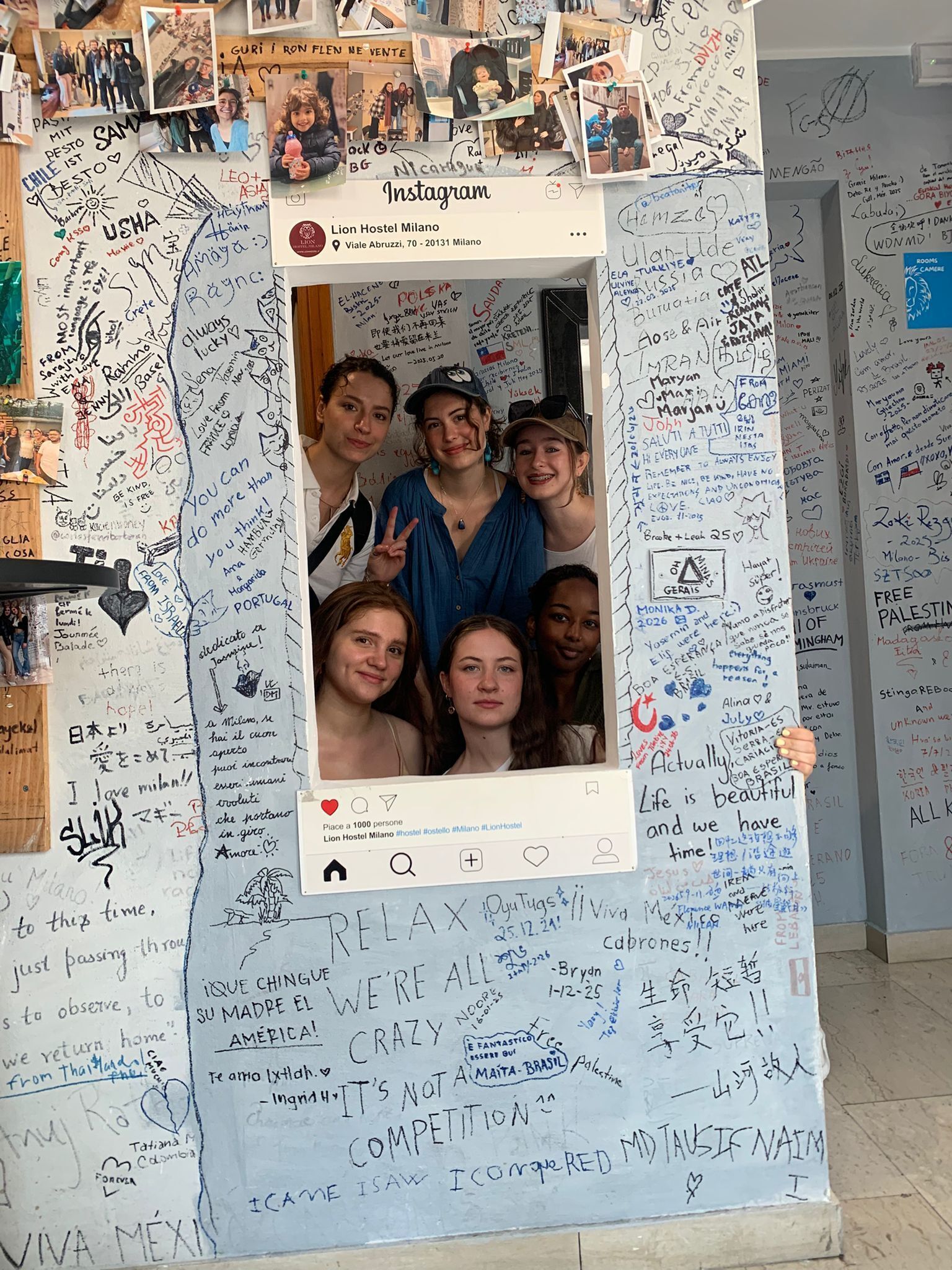 A wall with numerous handwritten messages and drawings, including a photo booth with a white frame and a social media post overlay.