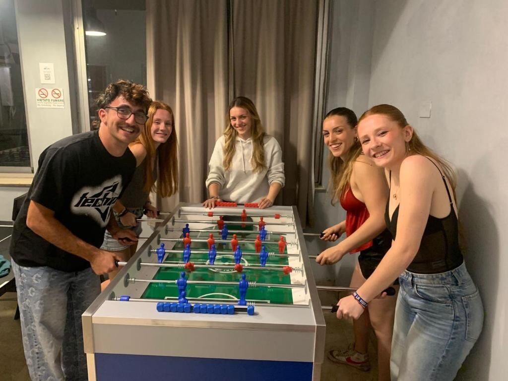 A group of people playing foosball in a room with a large window and curtains.