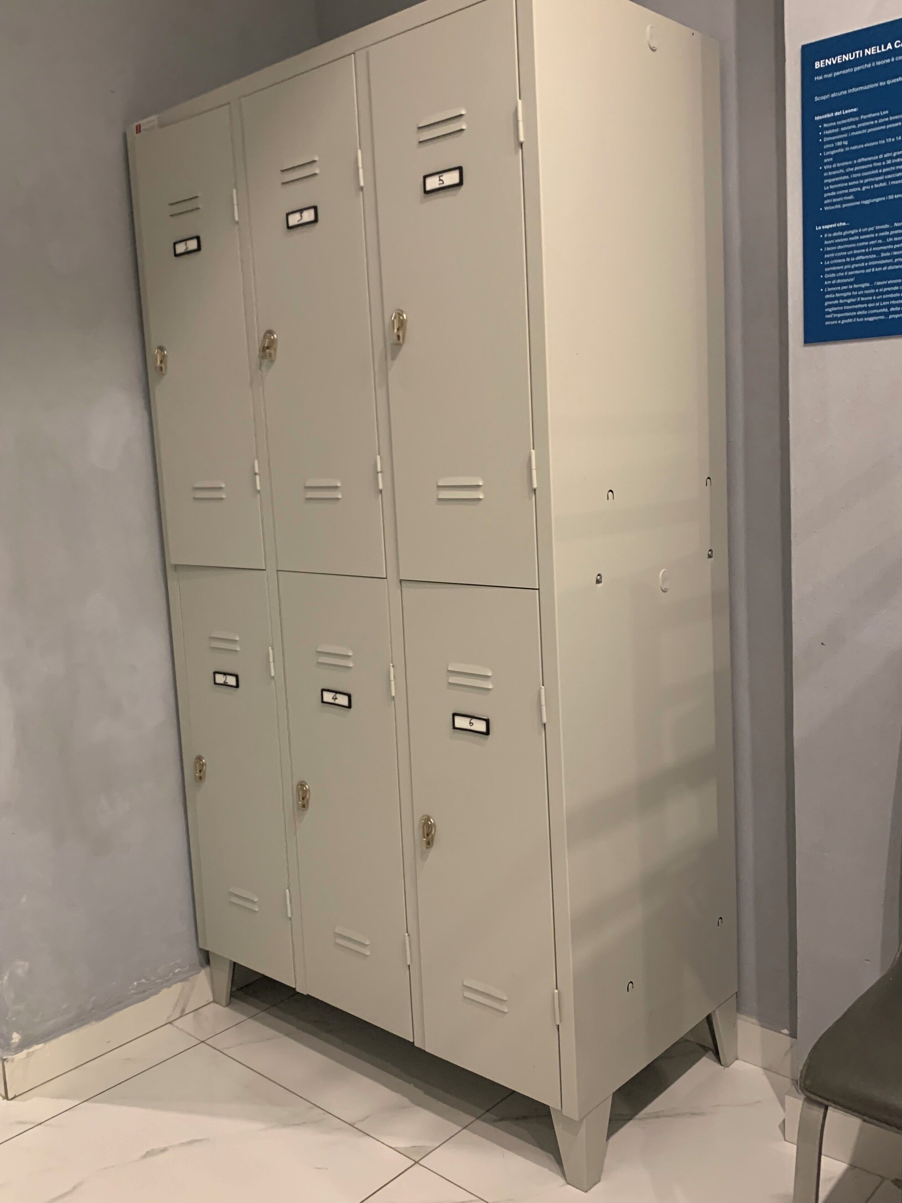 A set of six light-colored metal lockers with numbered labels, arranged in two columns against a wall.