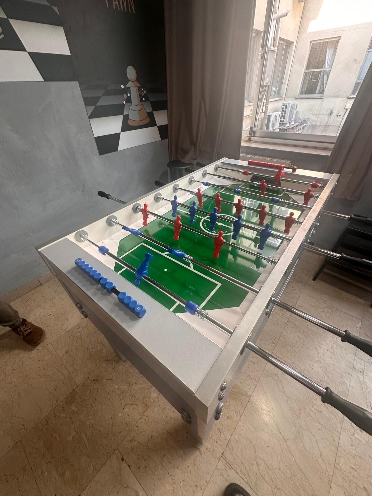 A foosball table in a room with a checkered wall and a window.