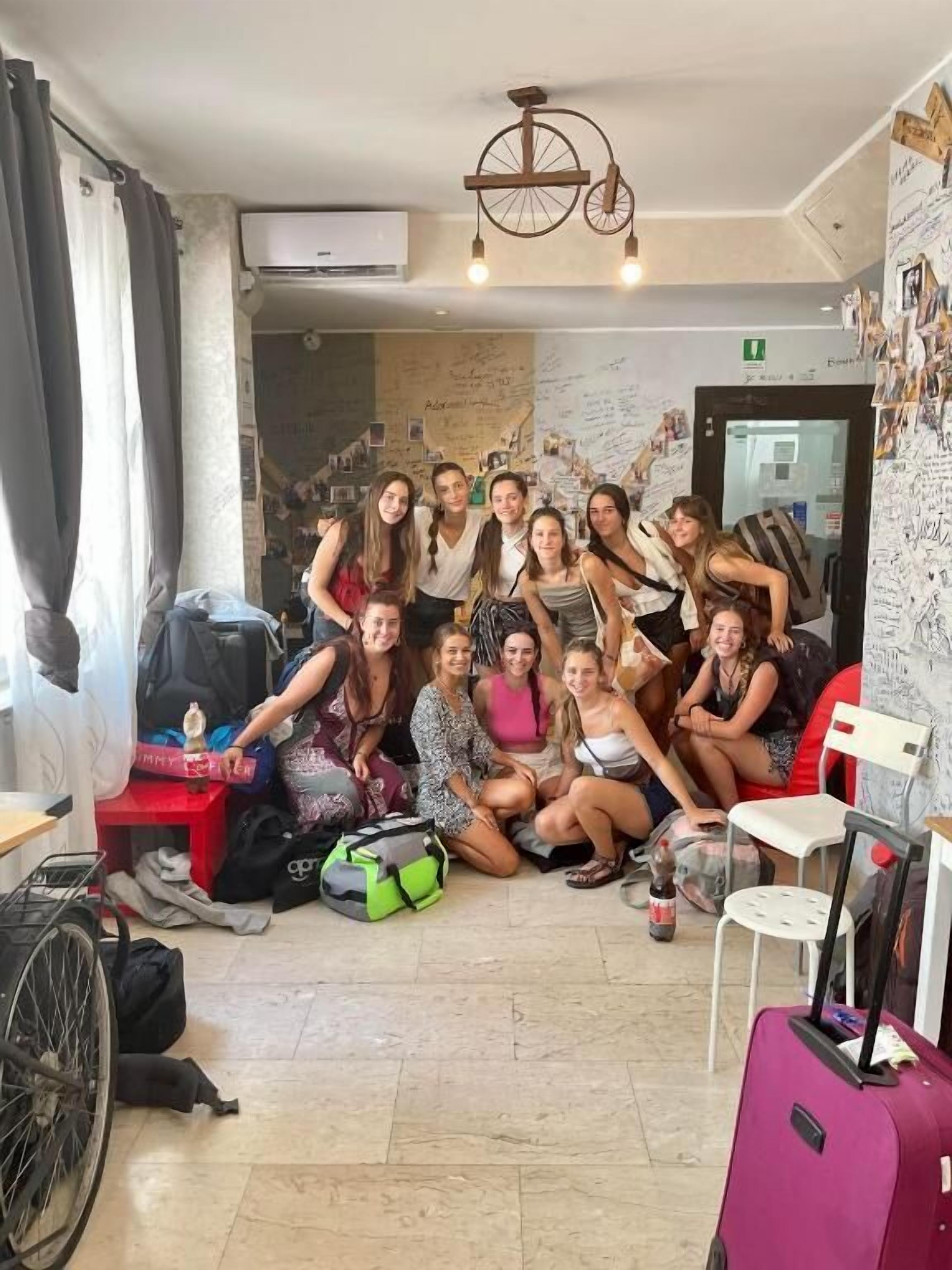 Un groupe de personnes se trouve dans une pièce où l’on aperçoit un fauteuil roulant, une chaise rouge et une valise.