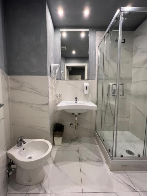 Un baño moderno con ducha envuelta en vidrio, lavamanos pedestal y bidé.