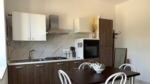Ett modernt kök med en väggbeklädnad av marmor, vita skåp, ett mörkt trämatbord och vita stolar.
