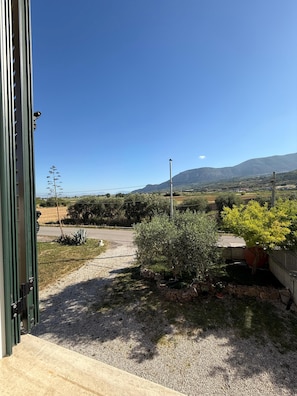 A view from inside a building looking out to a gravel path, greenery, and distant mountains. - Once upon a time (Capaccio Paestum)
