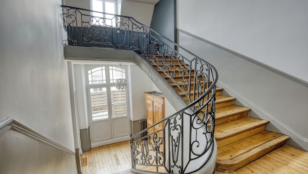 Una scala a chiocciola con ringhiere in metallo finemente decorate e gradini in legno, che conduce a un piano superiore.