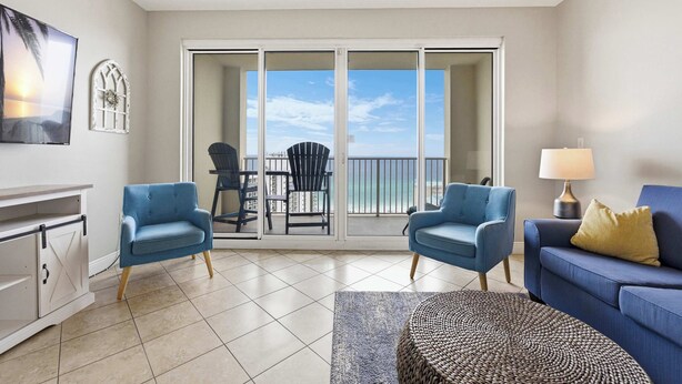 A living room with a view of the ocean, a balcony with chairs, and a sofa. - 20th Floor Condo With Stunning View (Miramar Beach)