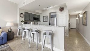 A modern kitchen with a central island, bar stools, and a dining area with a sofa and lamp. - 20th Floor Condo With Stunning View (Miramar Beach)