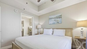 A bedroom with a large bed, a nightstand with a lamp, a painting on the wall, and a ceiling fan. - 20th Floor Condo With Stunning View (Miramar Beach)