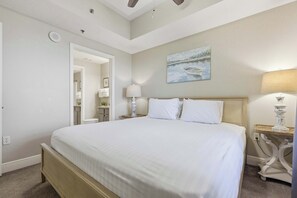 Ein Schlafzimmer mit einem großen Bett, einem Nachttisch mit Lampe, einem Bild an der Wand und einem Deckenventilator.