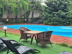 A swimming pool with lounge chairs and a table, surrounded by greenery. - Gatsby Ortosay (Bishkek)