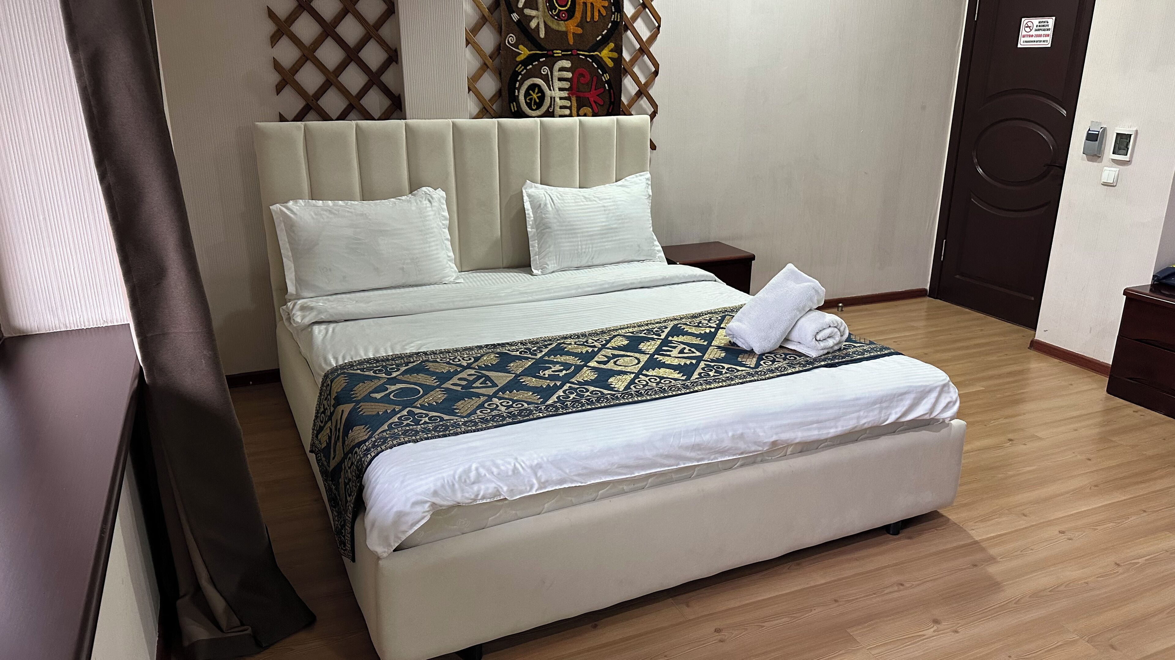 Una cama bien hecha con colcha estampada, cabecera y mesita de noche con lámpara.