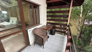A balcony with a wicker chair, a small table, and a trash bin.