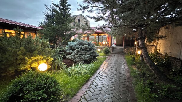 A paved pathway leading to a building with a red-tiled roof, surrounded by greenery and trees. - Gatsby Ortosay (Bishkek)