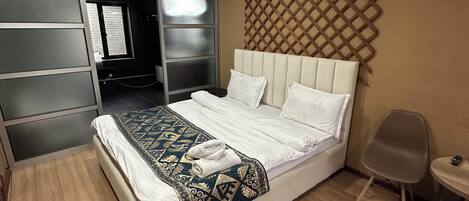 A bedroom with a bed, a wardrobe, a chair, and a wall-mounted TV.